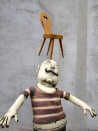 Ceramic Juggler Balancing A Hand Carved Chair